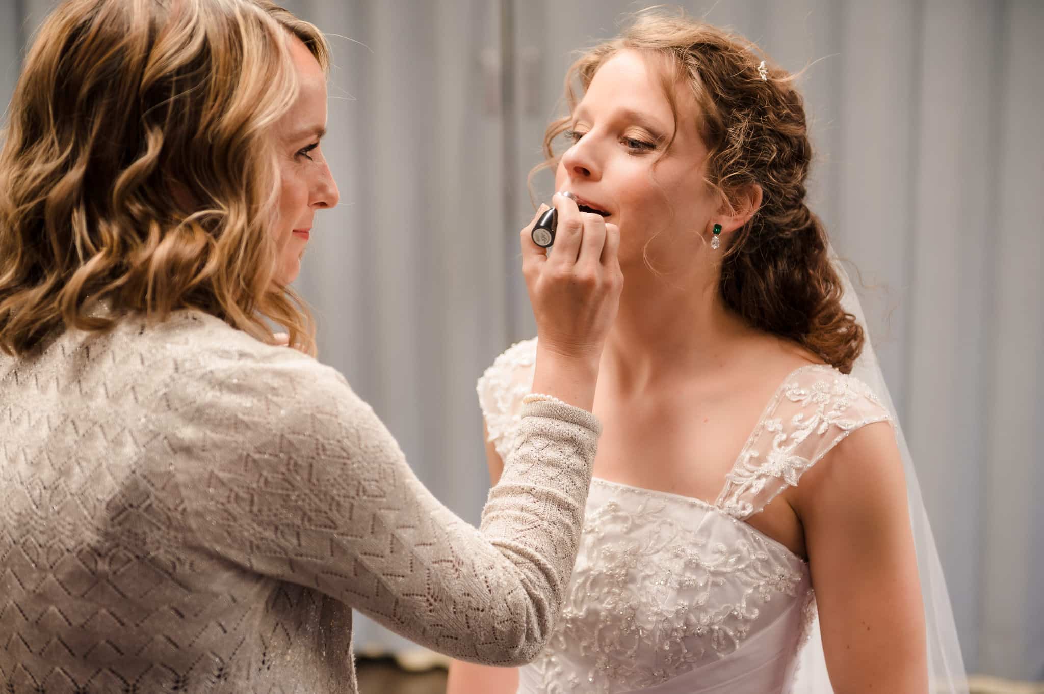 A friend applies lipstick to the bride helping her get ready before the ceremony.