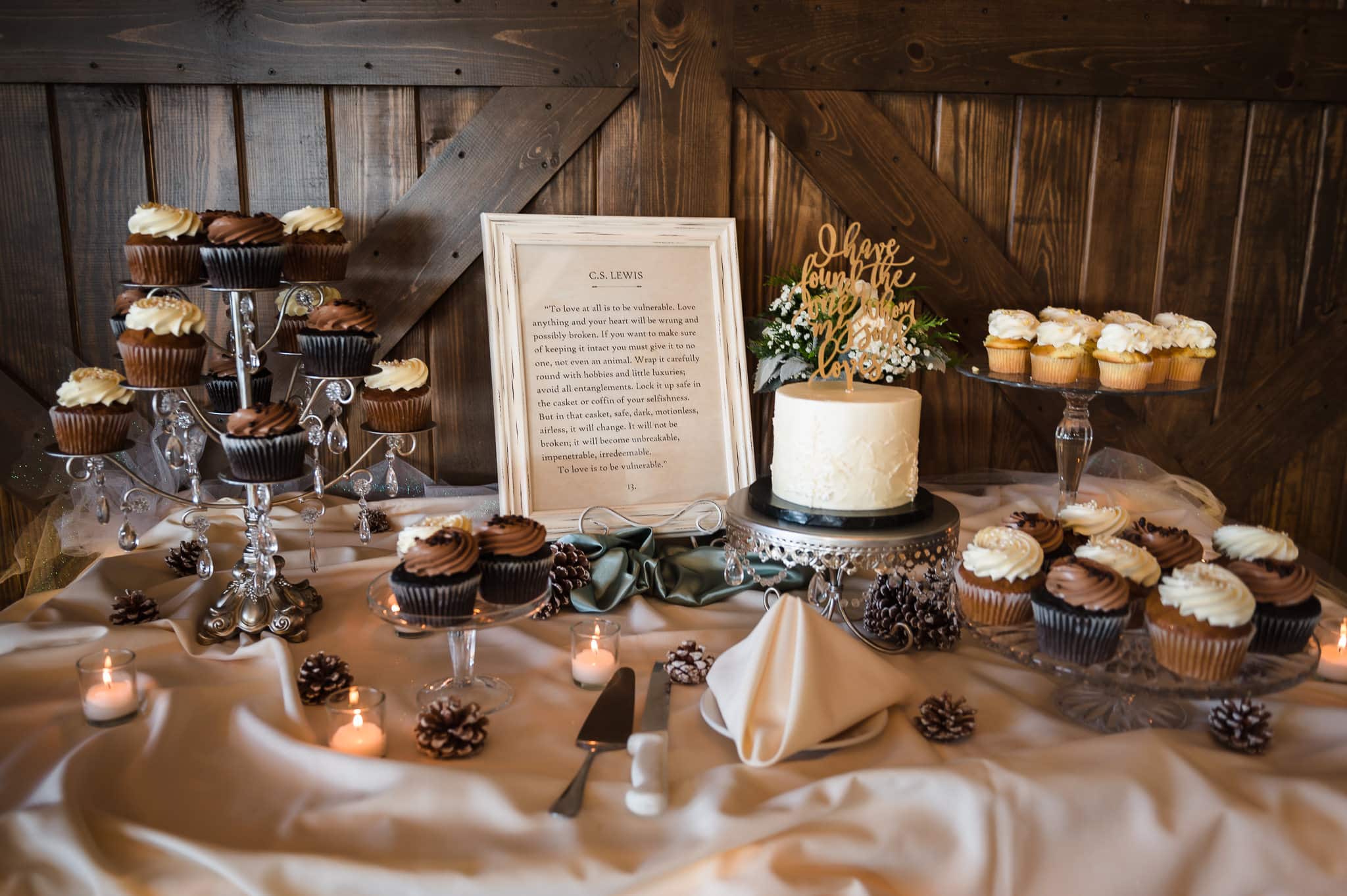 Dessert table with miniature white wedding cake, fudge and vanilla-topped cupcakes features a quote from CS Lewis about love.