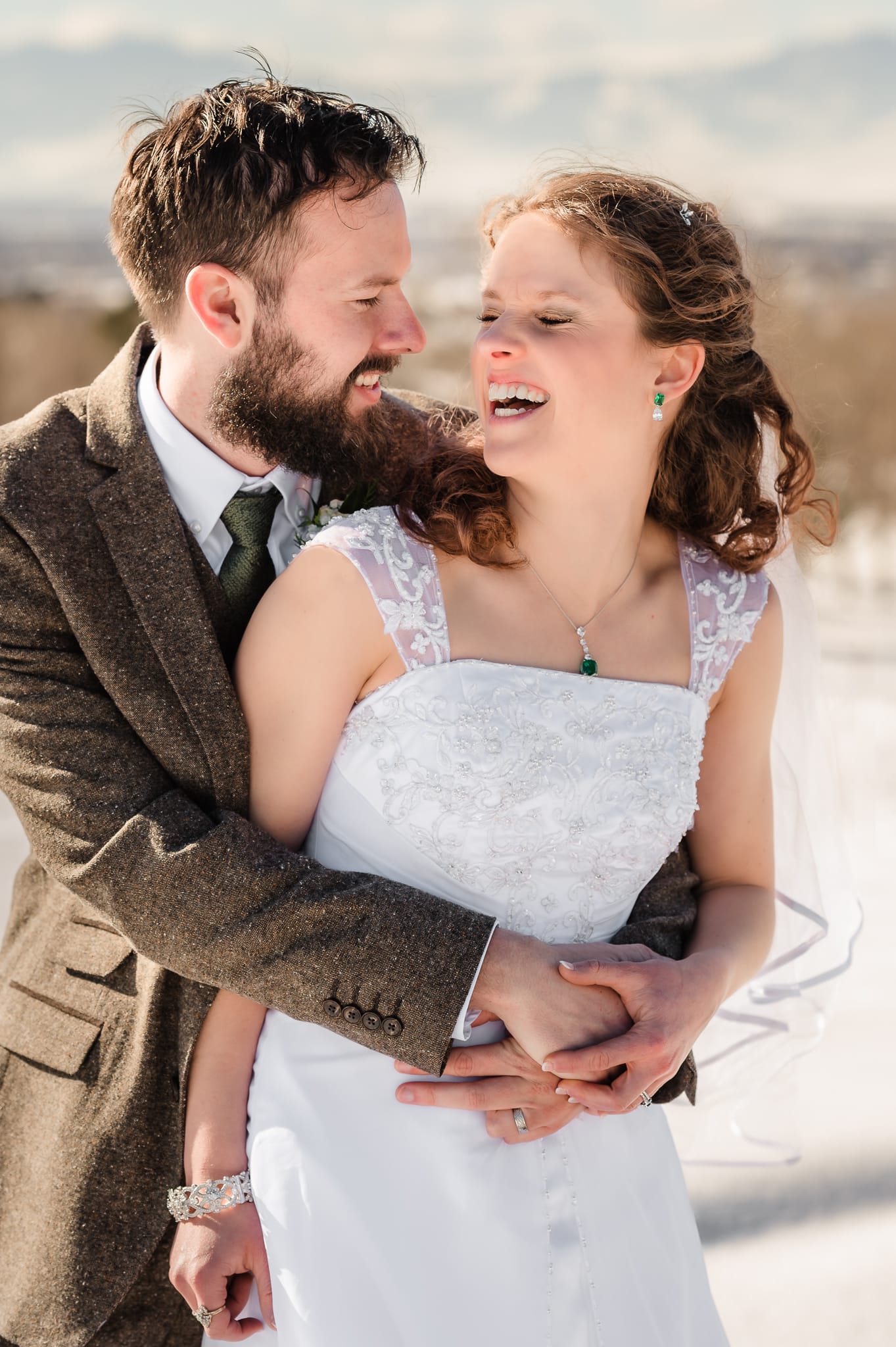 The groom holds his bride in the snow and they laugh together.
