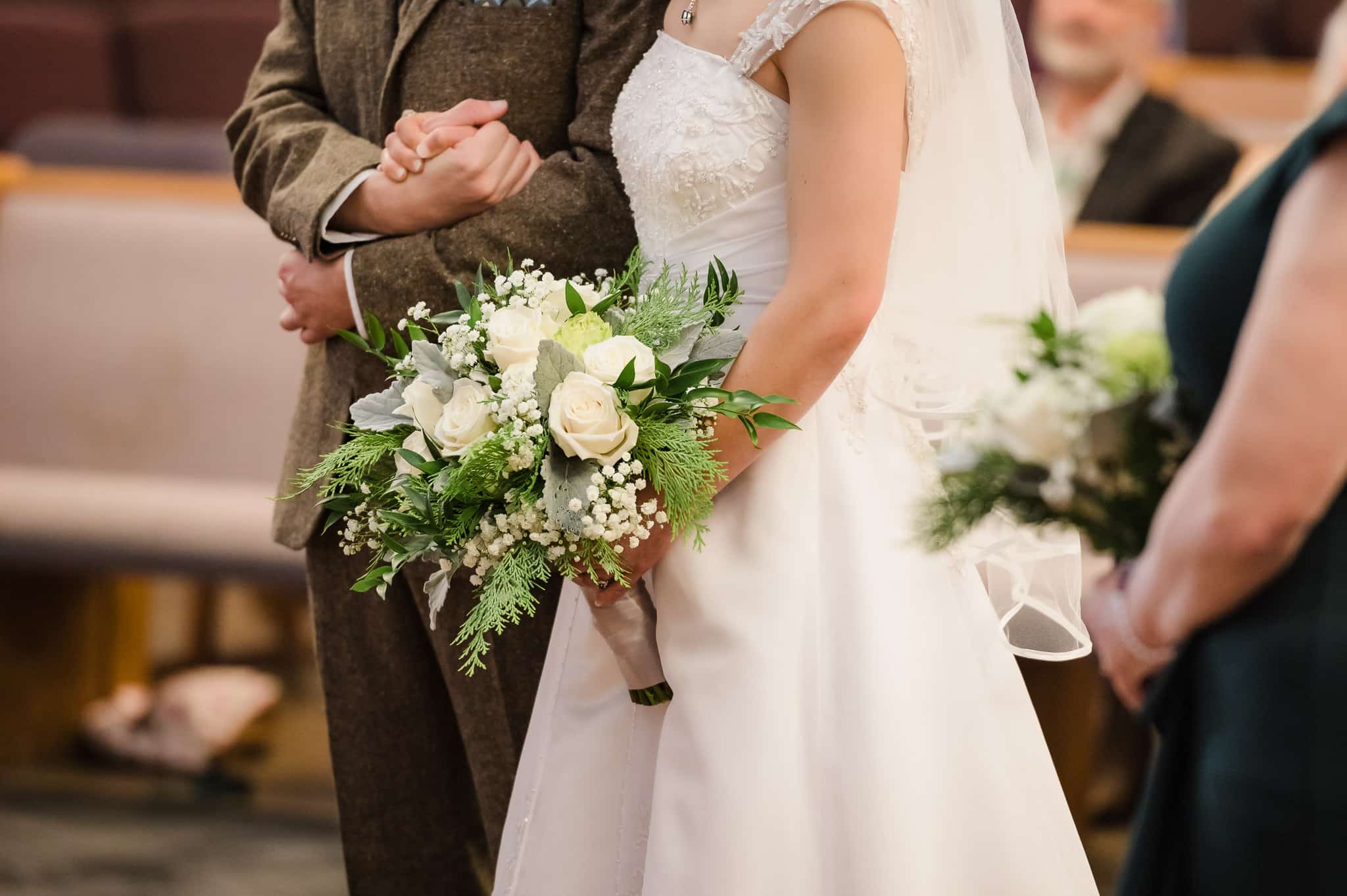 Close up of the bride and groom holding and squeezing their hands tightly together and the bridal bouquet.