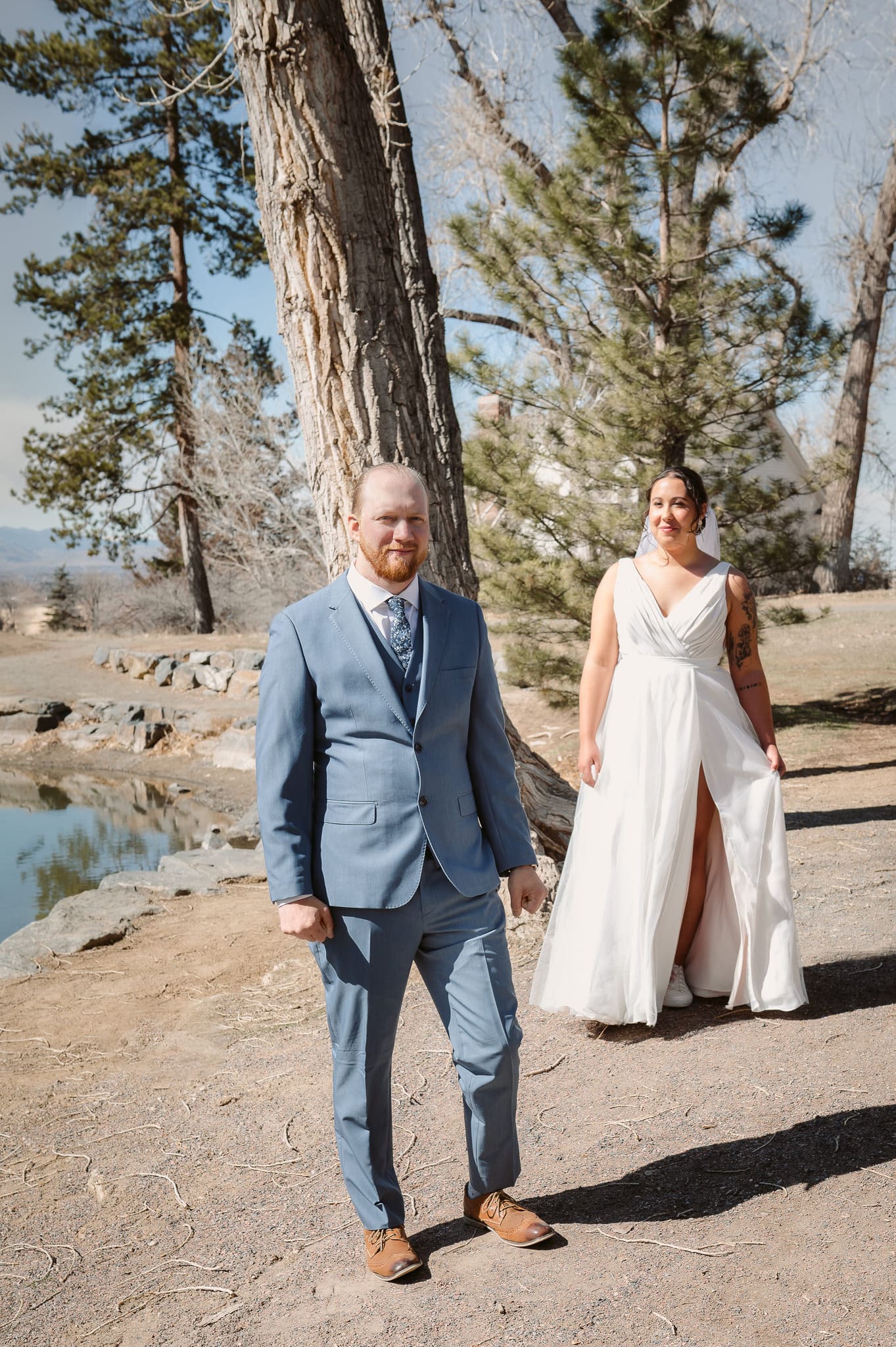 A man stands in a park with trees anticipating his wife-to be approaching quietly behind him for their first look.