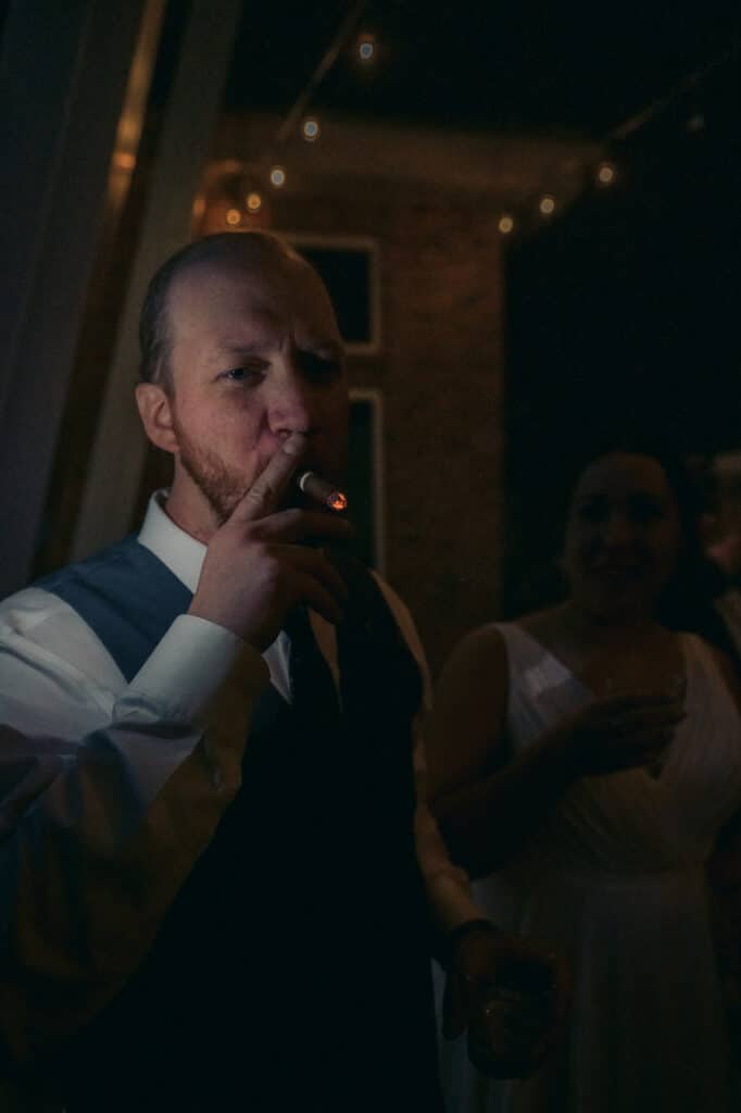 The groom enjoys a cigar outside in the near darkness.