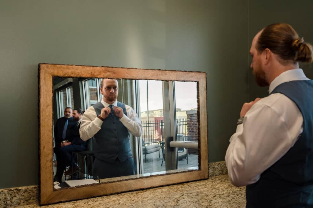 The groom straightens his tie in the mirror in the men's getting-ready area at Ashley Ridge.