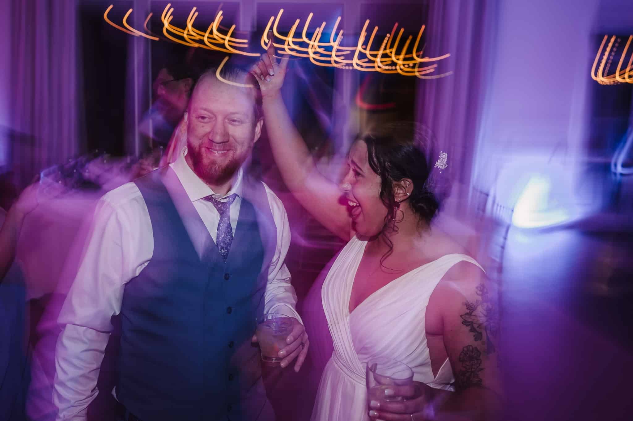 A motion-blur exposure of the bride and groom dancing creates swirls of purple, pink, and amber lights for a high-energy feeling.