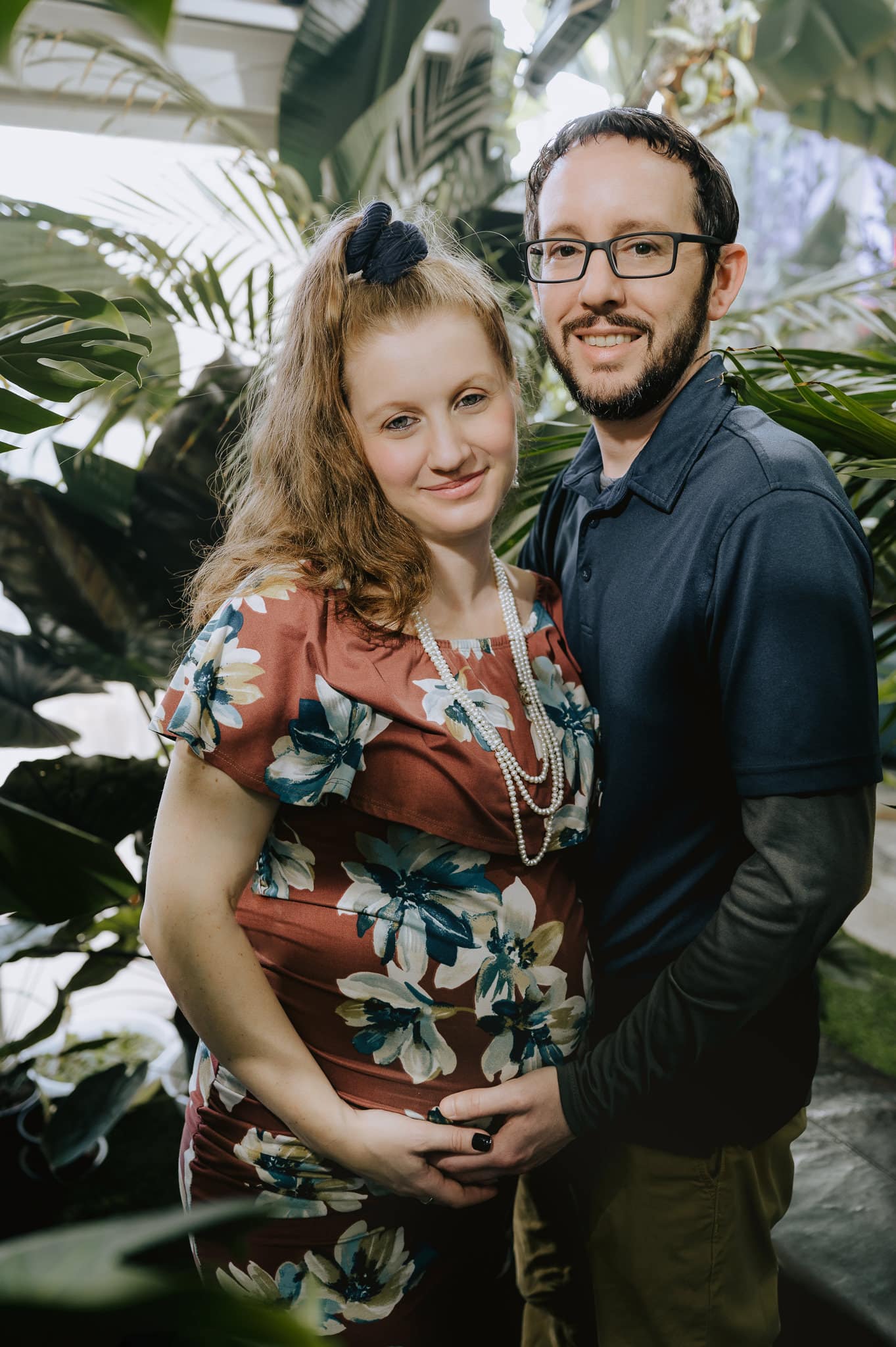 An expecting mother leans in close to her husband in a jungle portrait session.