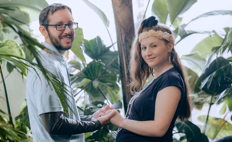 Expectant parents hold hands in a loft jungle during their maternity photo session.