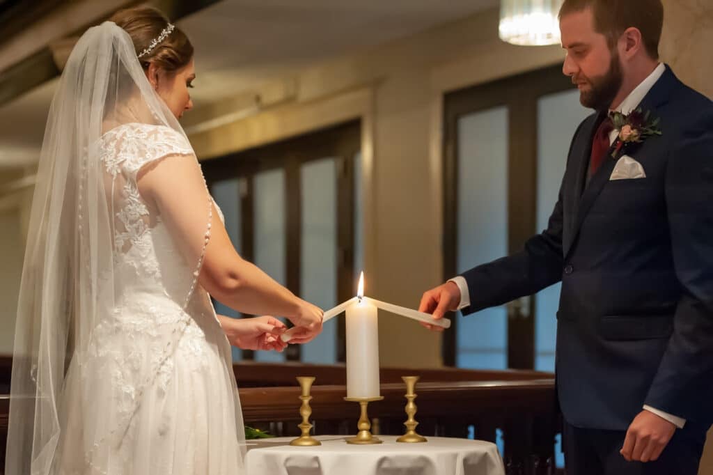A bride and a groom each light the unity candle with their own candles.