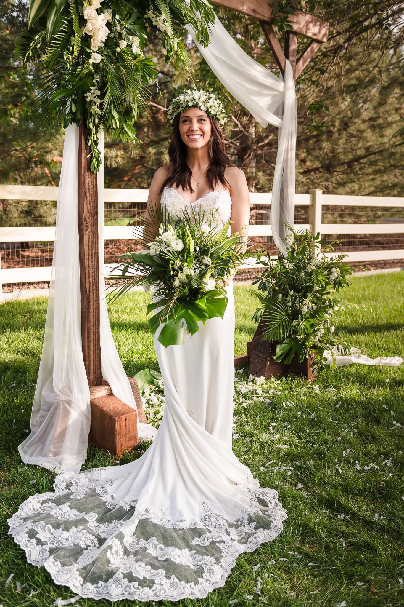 Bride in long dress with train and Hawaiian headpiece under and arbor.