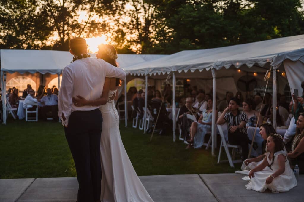 As the sun sets, vthe bridal couple look out at their guests inside tents as the toasts are going on.