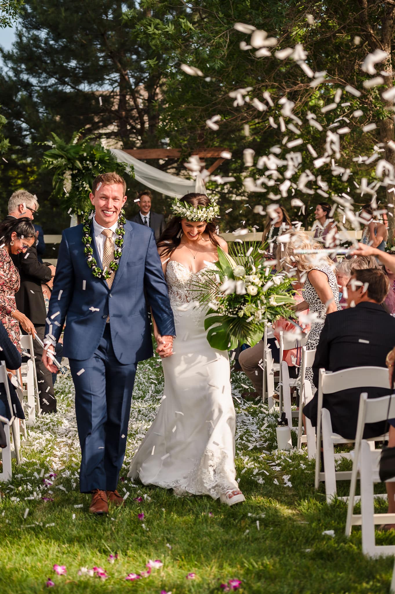 A bride and groom hold hands and walk through a storm of paper created during a confetti exit.