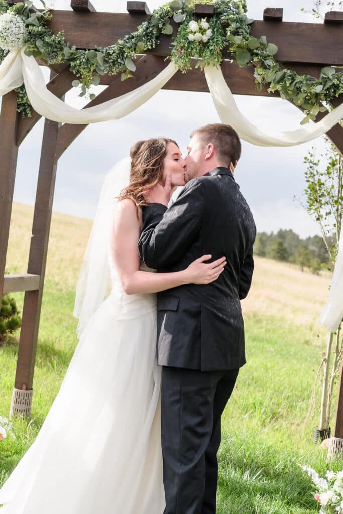 A recently married couple kisses for the first time after their outdoor ceremony at 1C Barn in Monument, Colorado