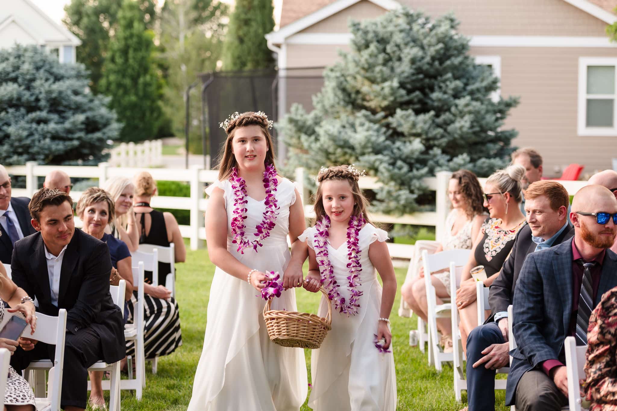The flower girls wearing brightly colored leis walk down the wedding aisle with a basket and toss petals on the ground.