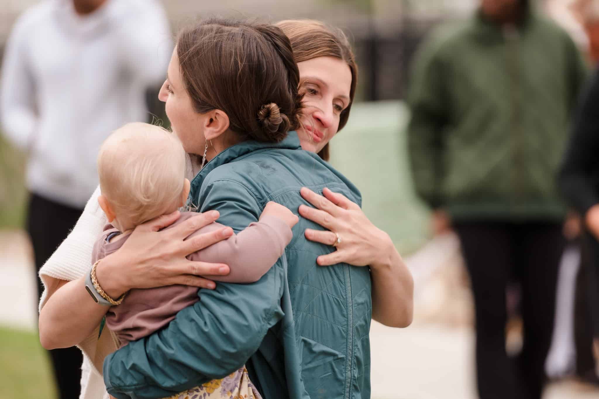 Two women and a baby give each other a hug during an emotional moment at a going away party.