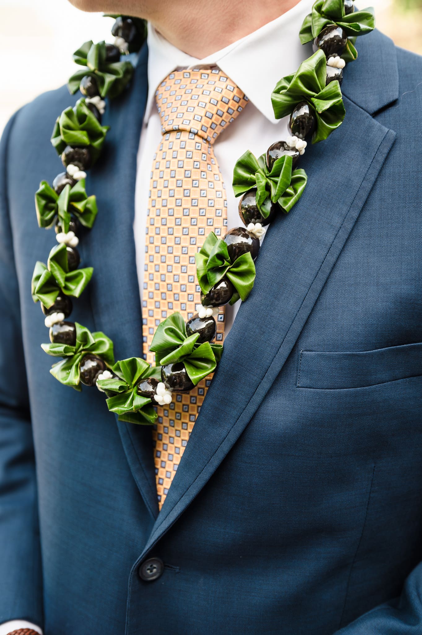 Close up of a lei with kukui and greenery on a groom.