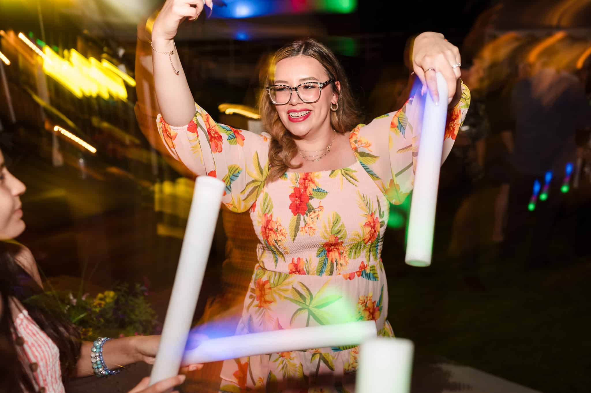 A guest holding glow sticks dances at the wedding reception.