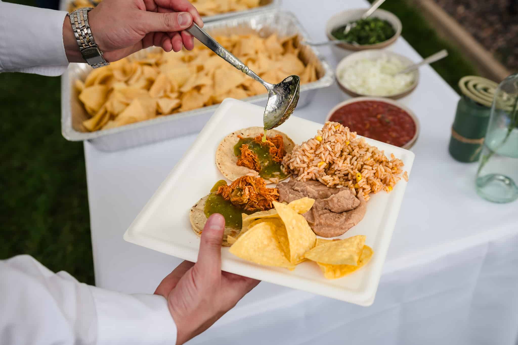 A guests serves up a plate of tacos and adds one of many available sauces on the top.