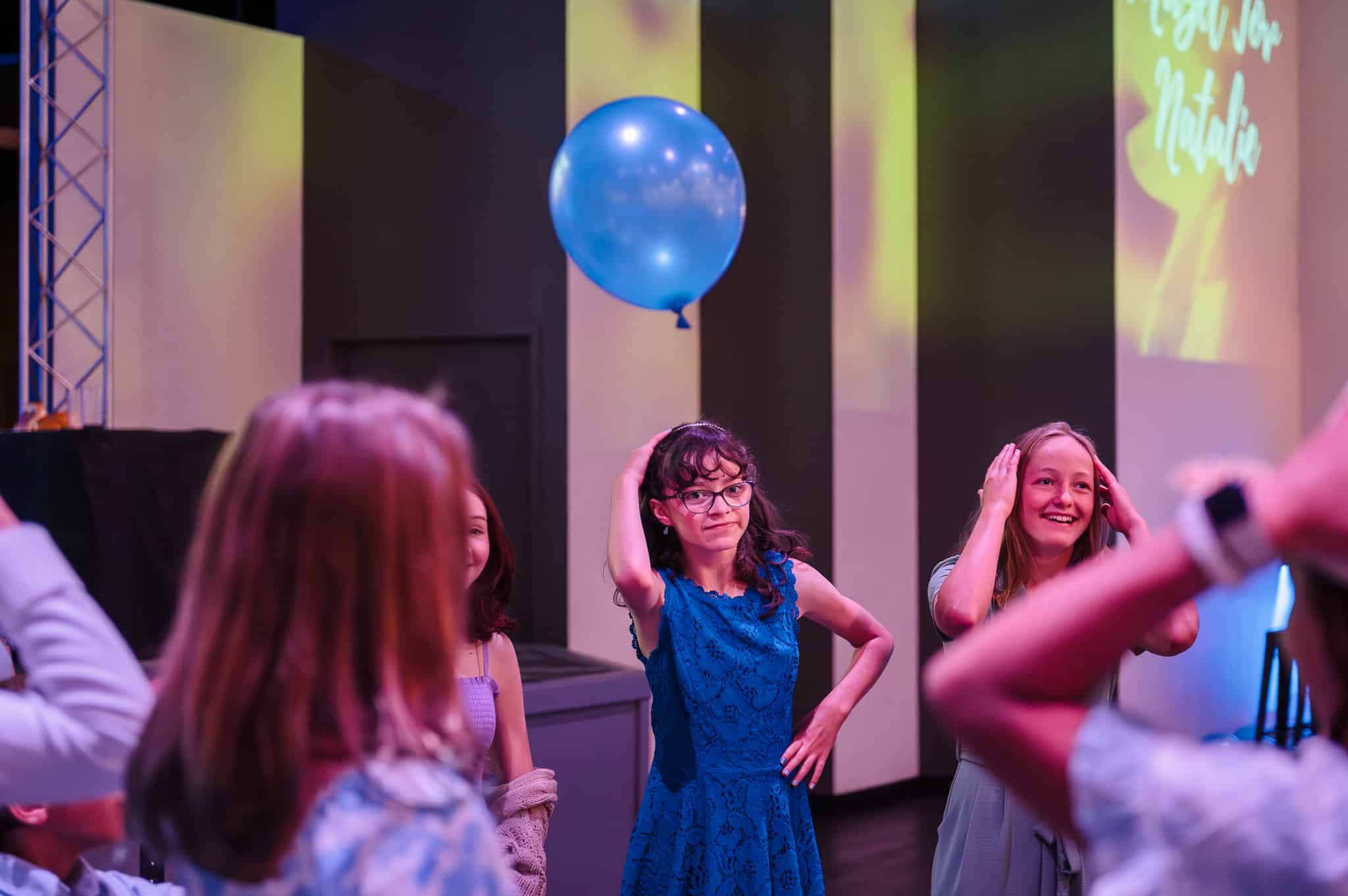 Young teens attempt to keep balloon airborne and dance the macarena during a bat mitzvah.