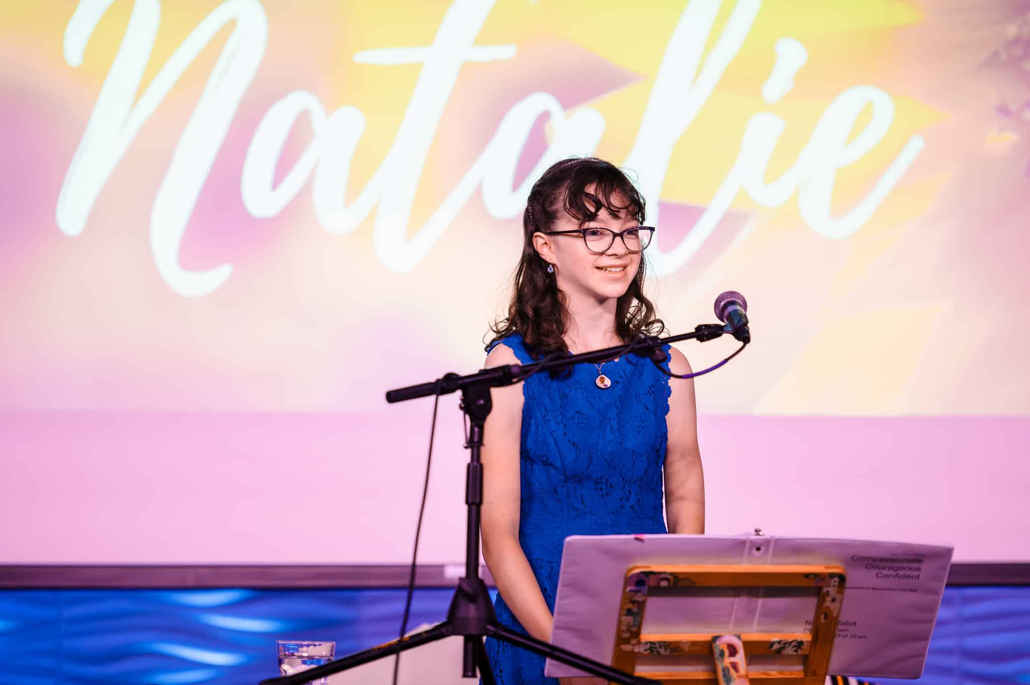 A young woman at her mitzvah with a project screen showing her name, "Natalie."