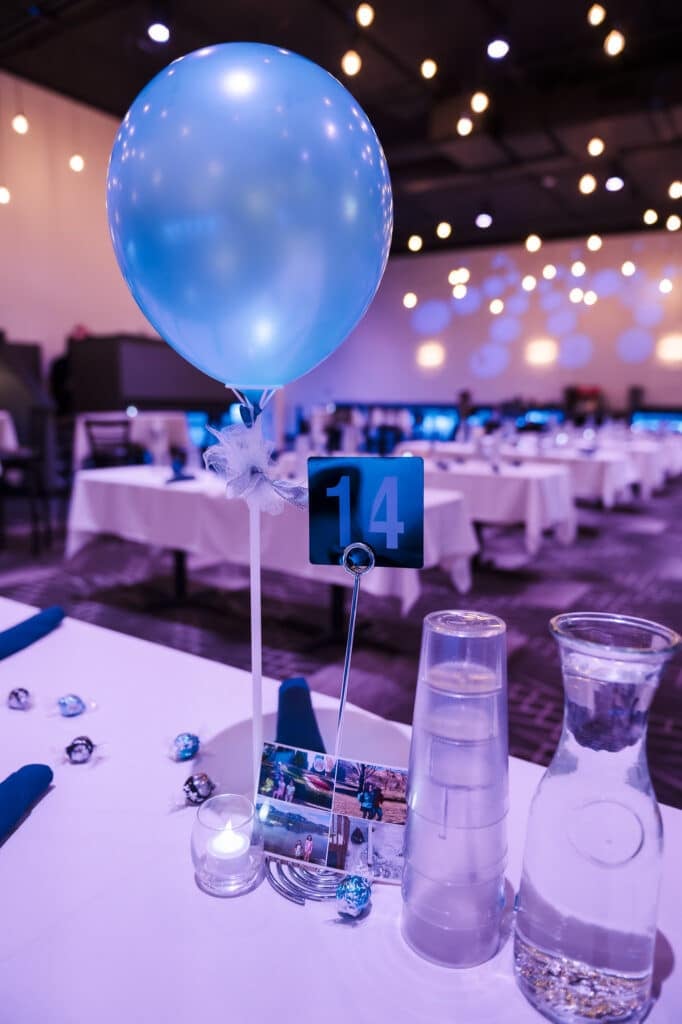 View of an event table set with blue napkins and table number 14. The rest of the many tables are blurred in the background.