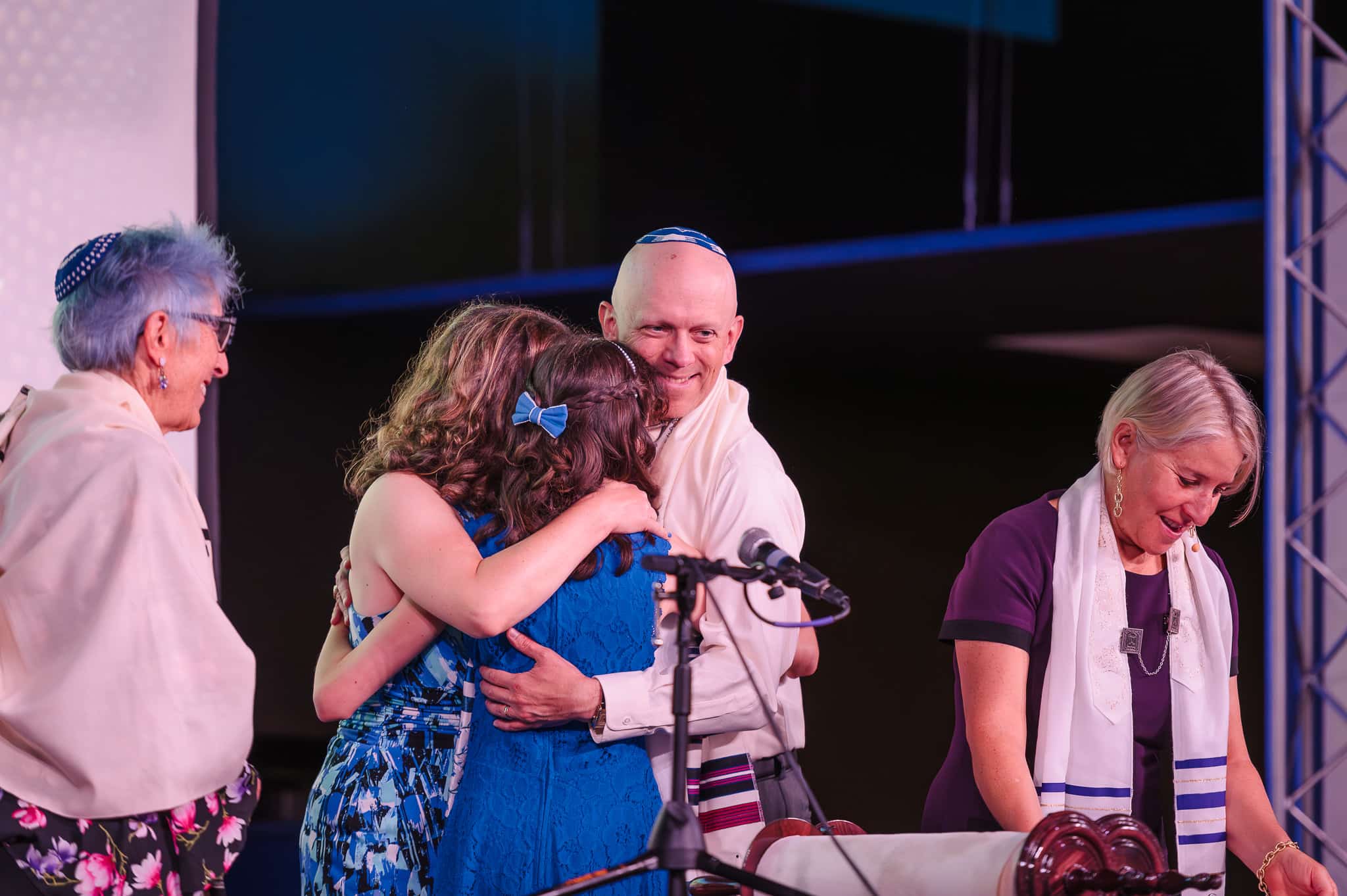 A young woman is hugged by her parents at a bat mitzvah service.