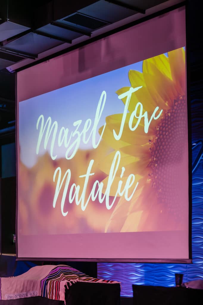 Nissi's event center features several projection screens like this one that says, "Mazel Tov Natalie" over a sunflower.