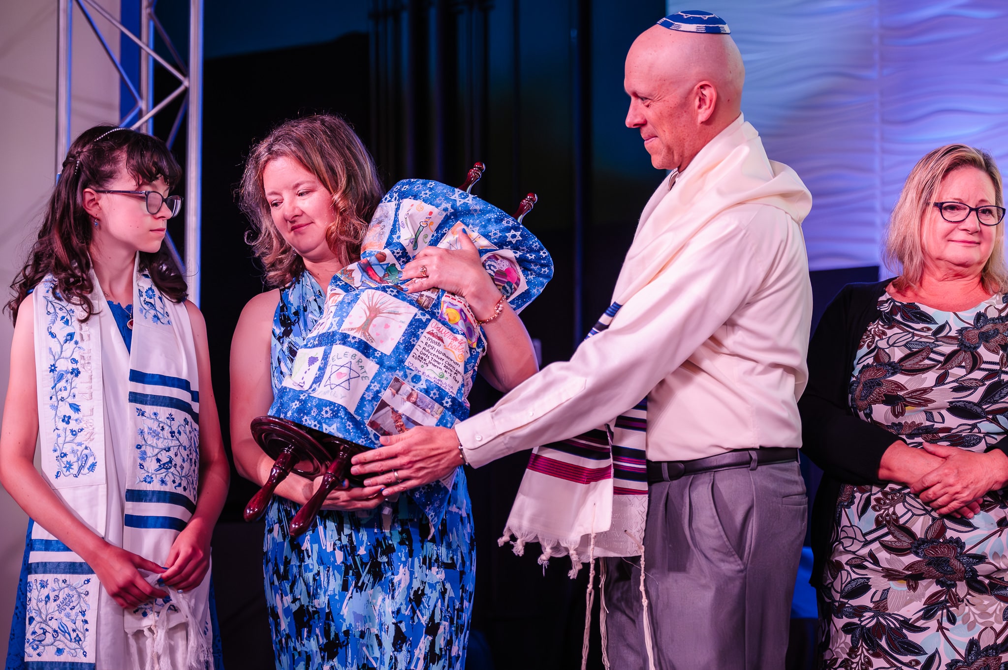 A woman receives The Torah from her husband and prepares to pass it to their daughter during a mitzvah service.
