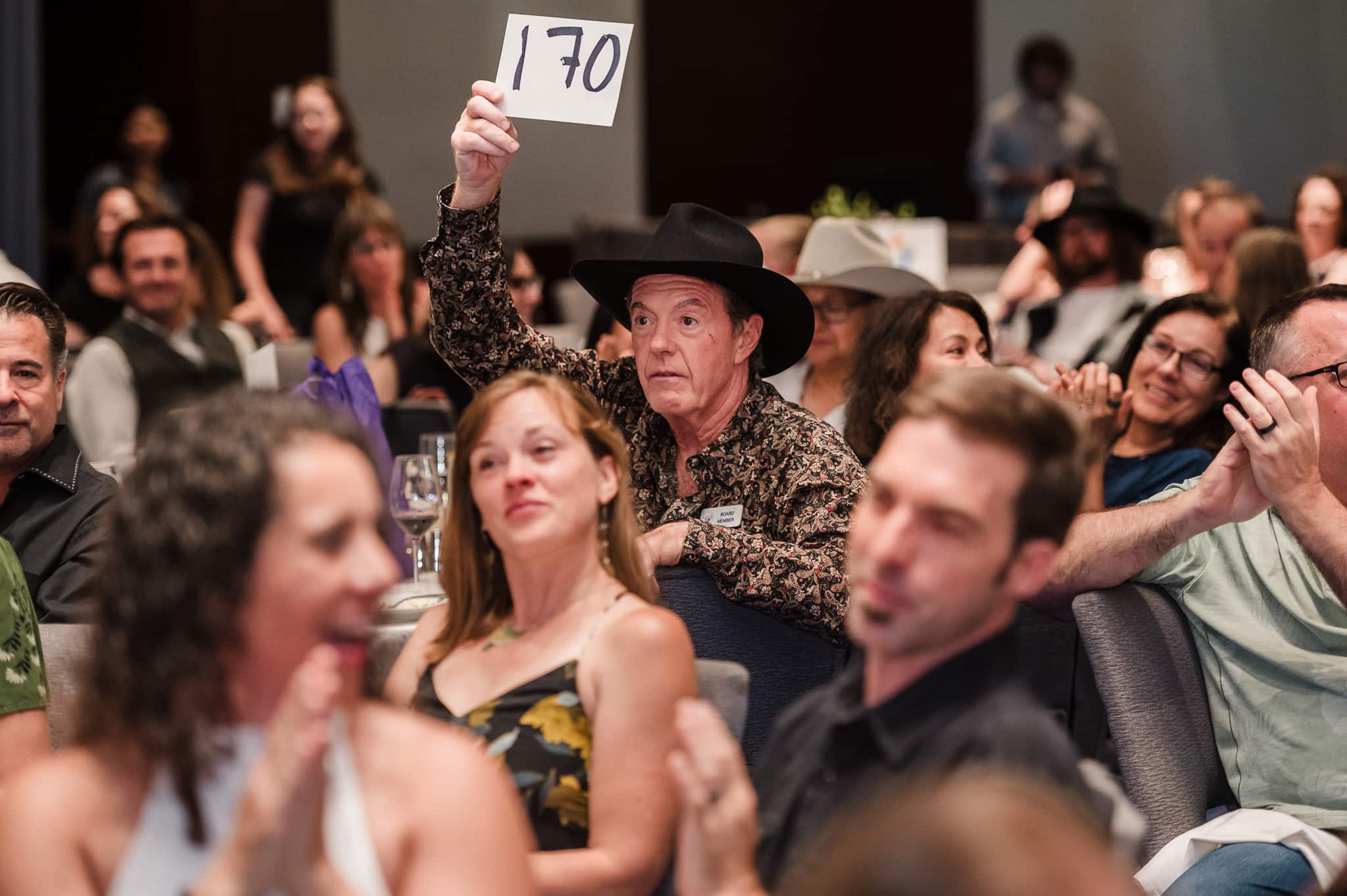 A man in a cowboy hat raises his bidding number during a charity auction fundraiser.