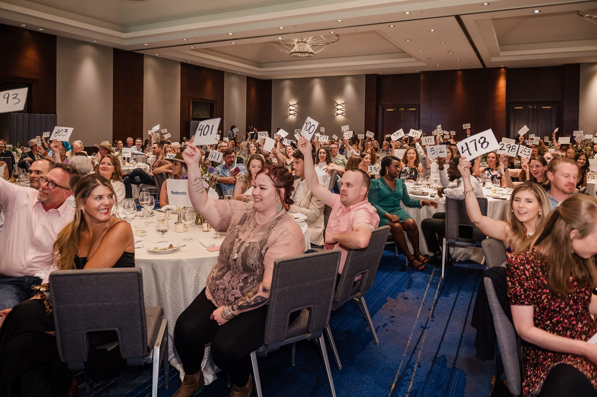 A wide view of people holding up their bidding numbers during a charity fundraiser.