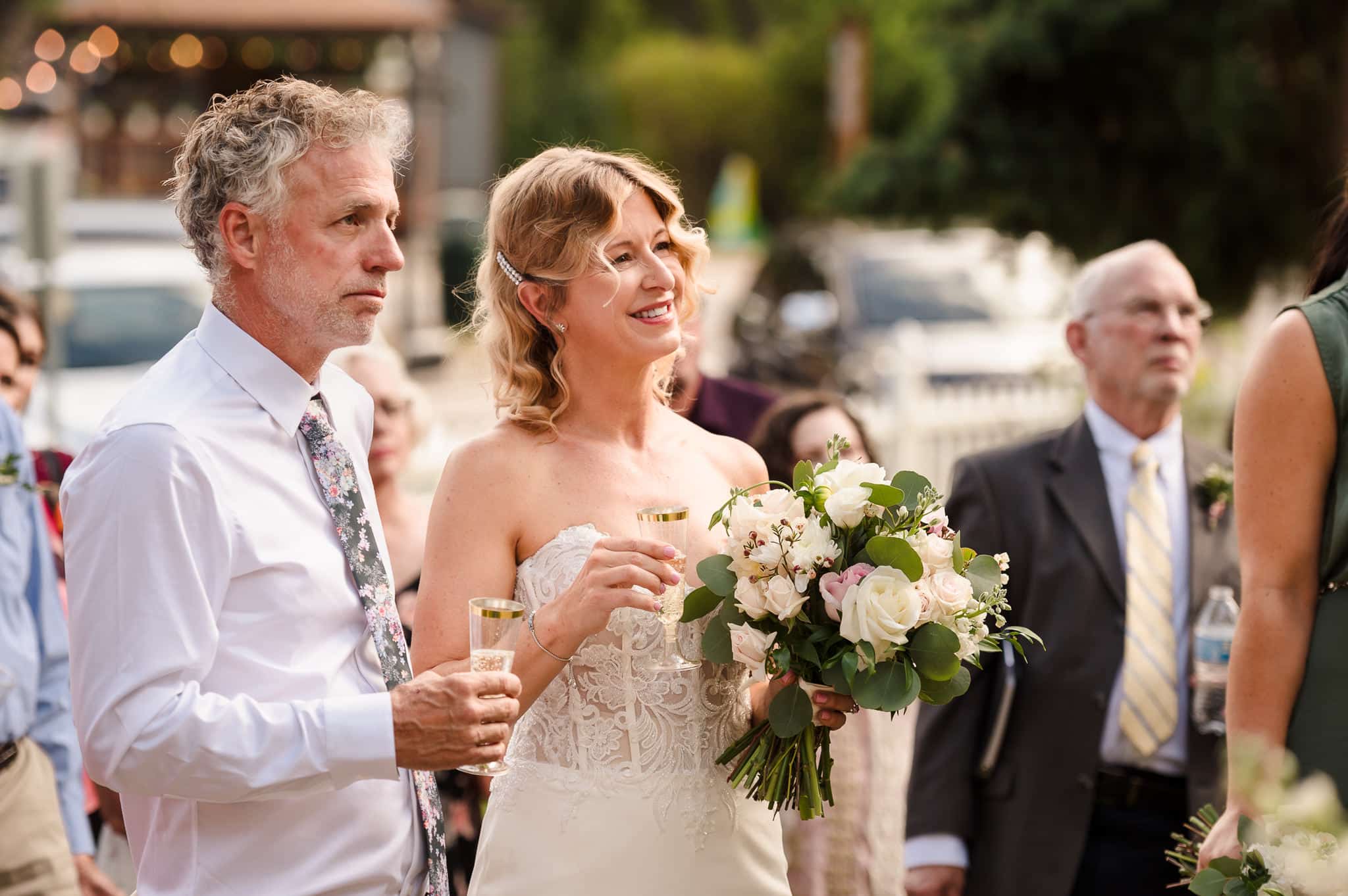 The bride and groom stand side by side holding champagne glasses and listen to the toast being given in their honor.