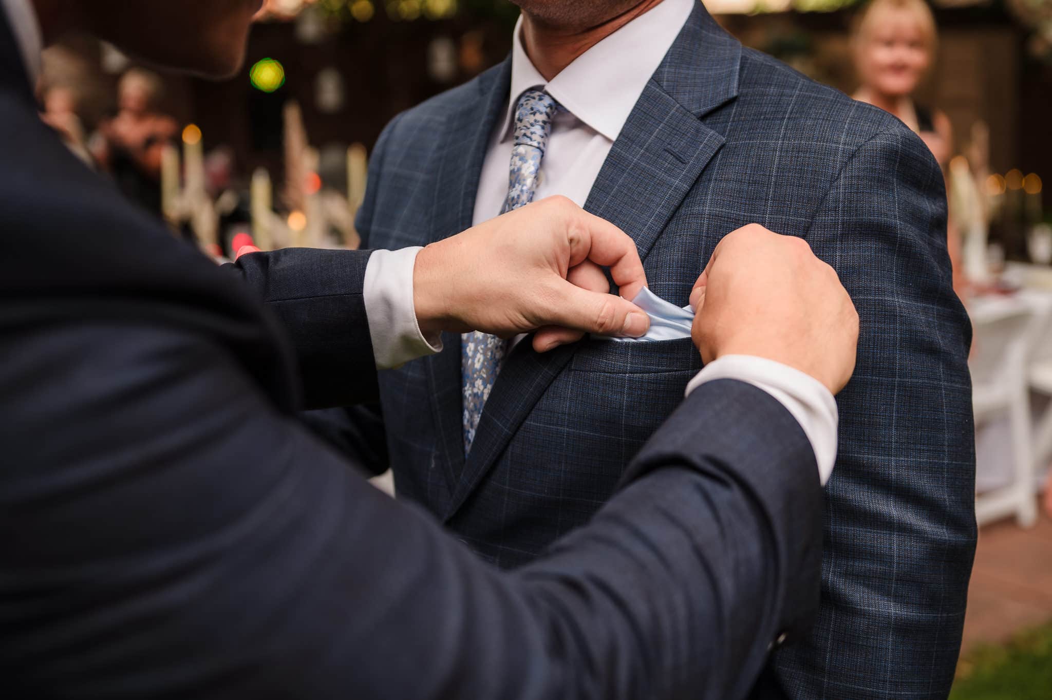 Close up of a hands adjusting the pocket square in the suit of a groom.