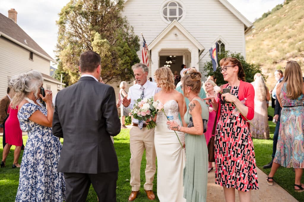 The bride and groom engage in conversation with their guests outside the little white church where they just married.