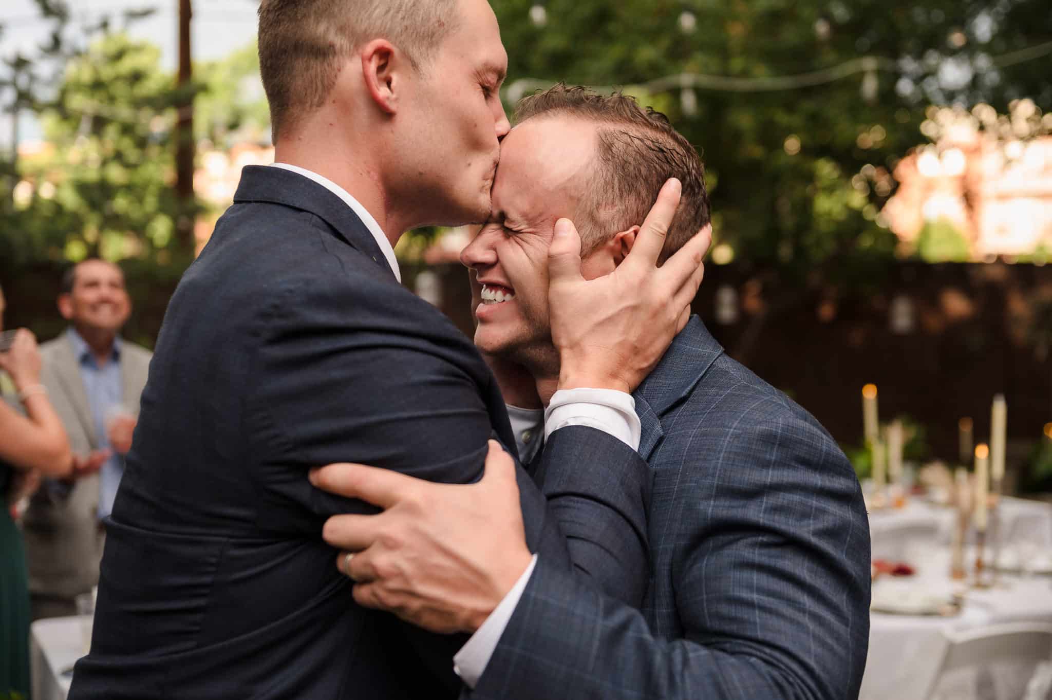 The groom receives a kiss from a bro on the forehead.