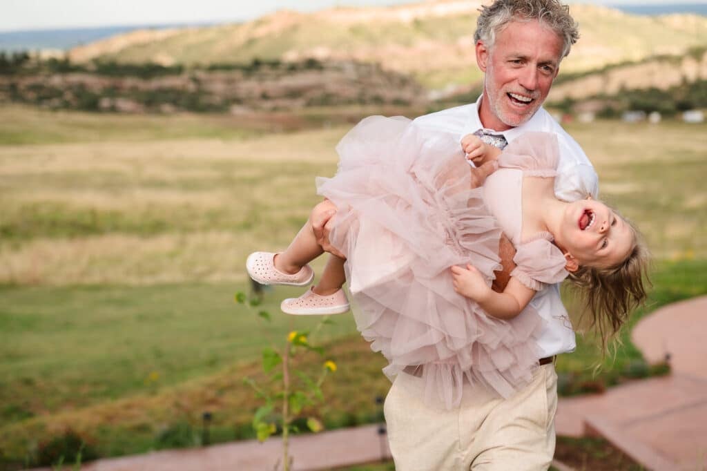 The groom holds his laughing granddaughter at his wedding reception.