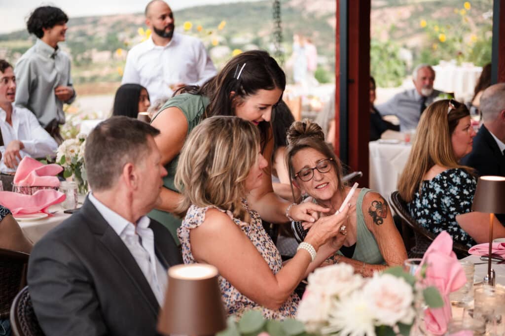 Guests look at photos on a cell phone during a wedding reception.