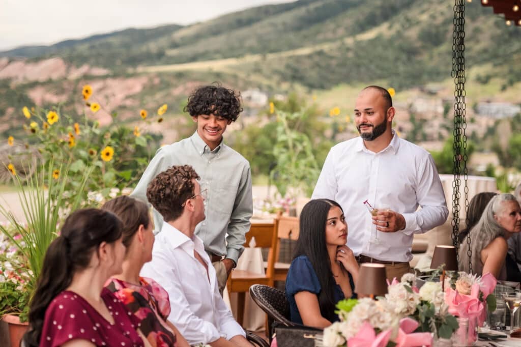 Guests at a wedding, some seated and other standing, converse and relax at a reception.