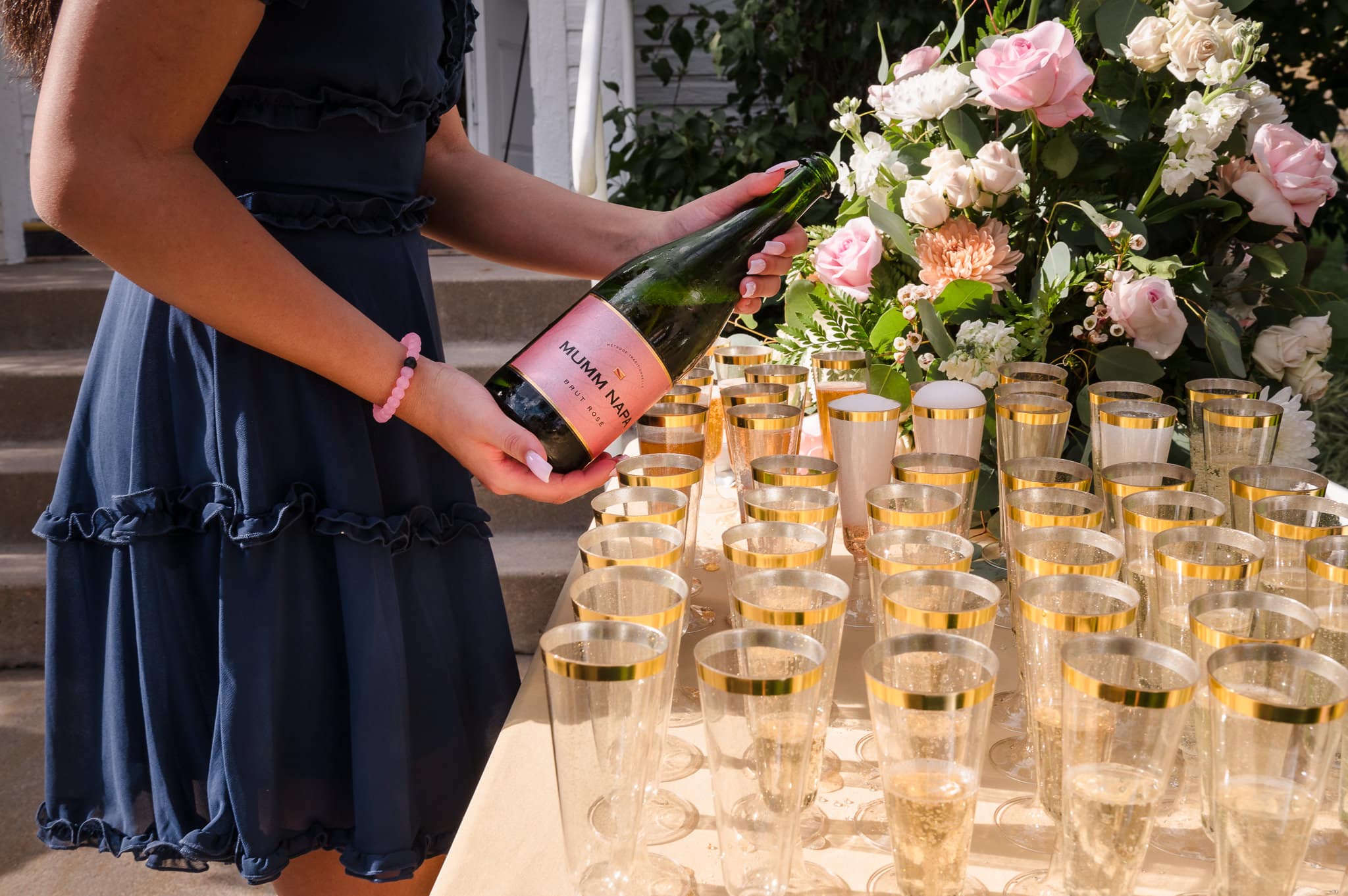A young woman pours champagne into glasses set on a table after a wedding.