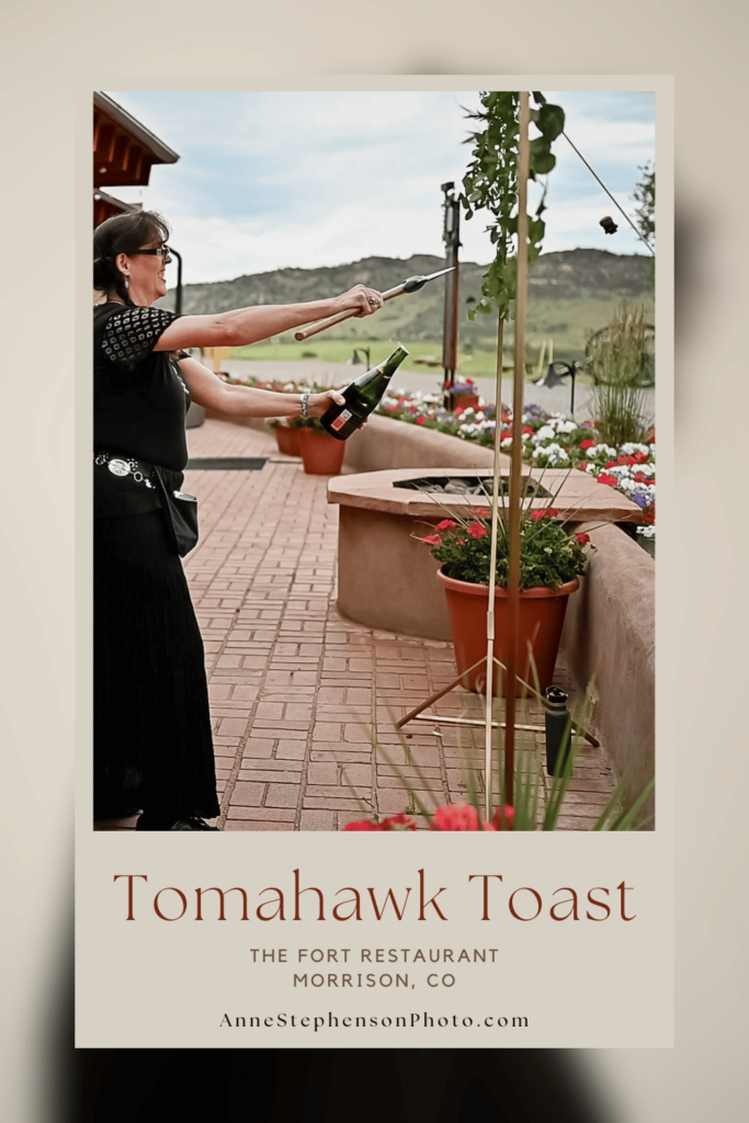 Pinterest Pin showing the Tomahawk Toast at The Fort in Morrison - A woman uses a tomahawk to remove the cork from a champagne bottle.