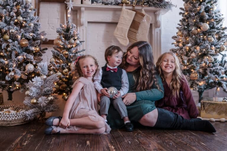 A mother, her two daughters and sons sit in front of a fireplace during a family photo mini session.