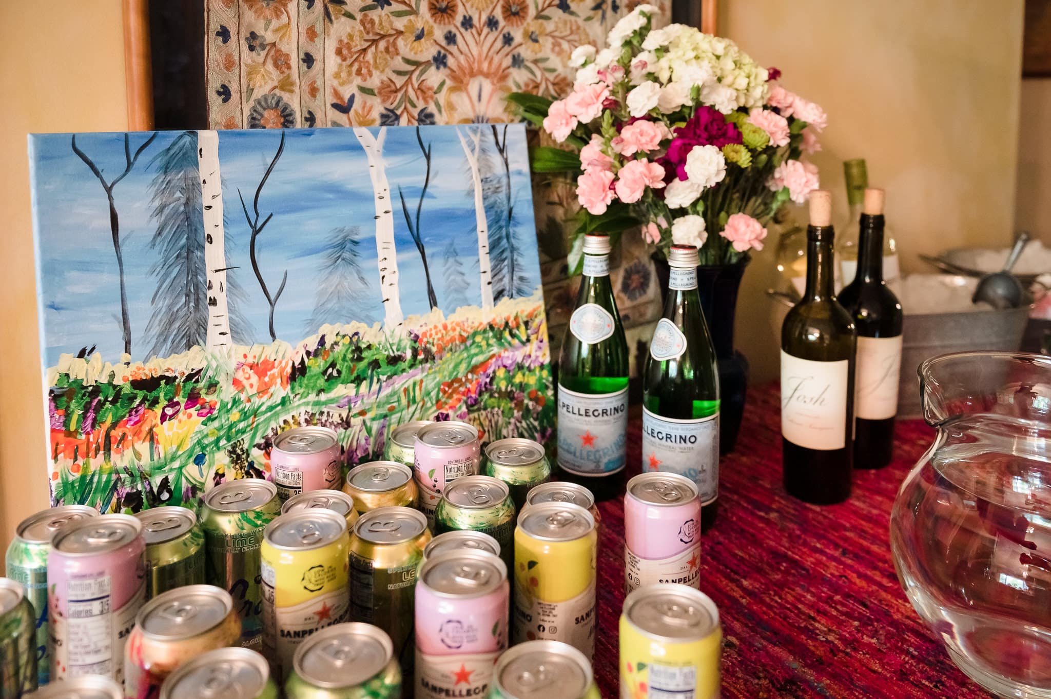 A painting decorates a beverage table filled with cans and bottles of water and sparkling water.