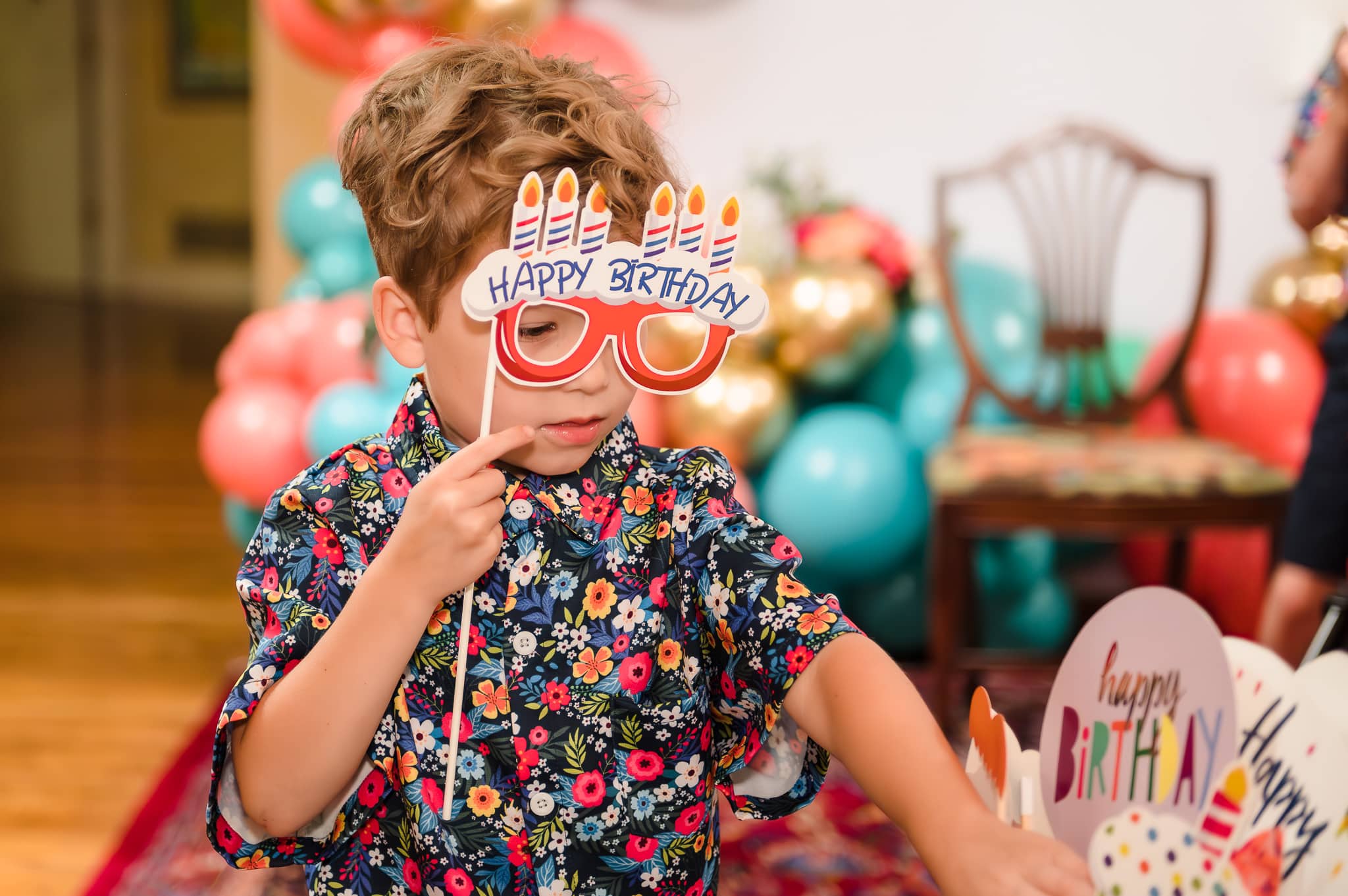 A little boy holds a pair of fun glasses that say "happy birthday" for a photo booth at a senior birthday party.