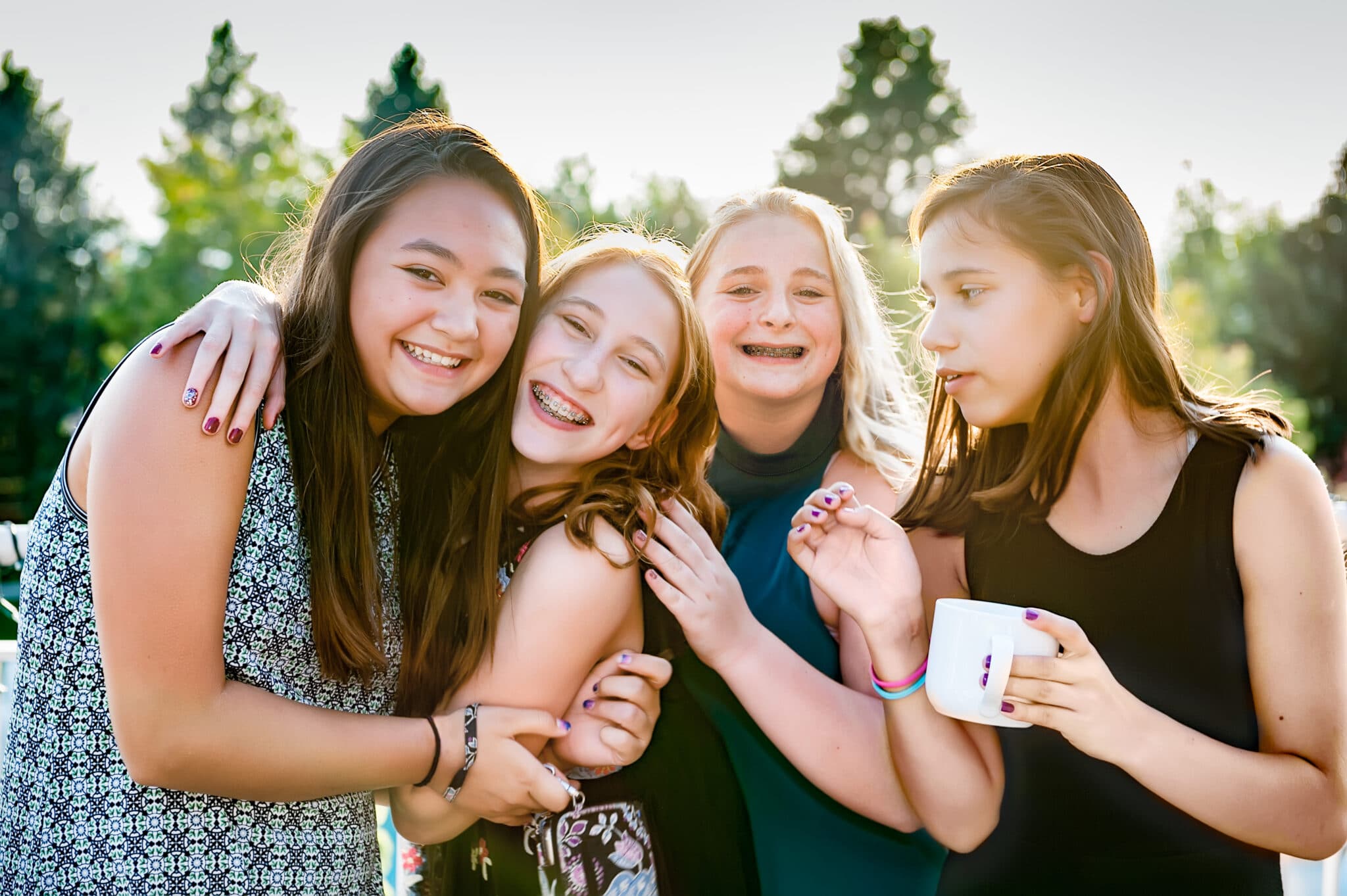Four young girls backlit by the sun hug each other during the bat mitzvah.