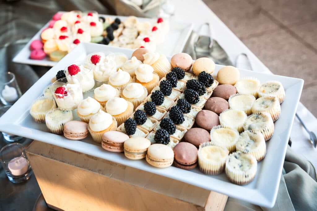 A tray of catered desserts beautifully topped with whipped cream, raspberries and blackberries in neat rows on a tray at a bat mitzvah.