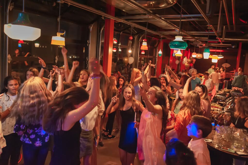 Guests pack the dance floor and raise their arms as they sway to music at a bat mitzvah.