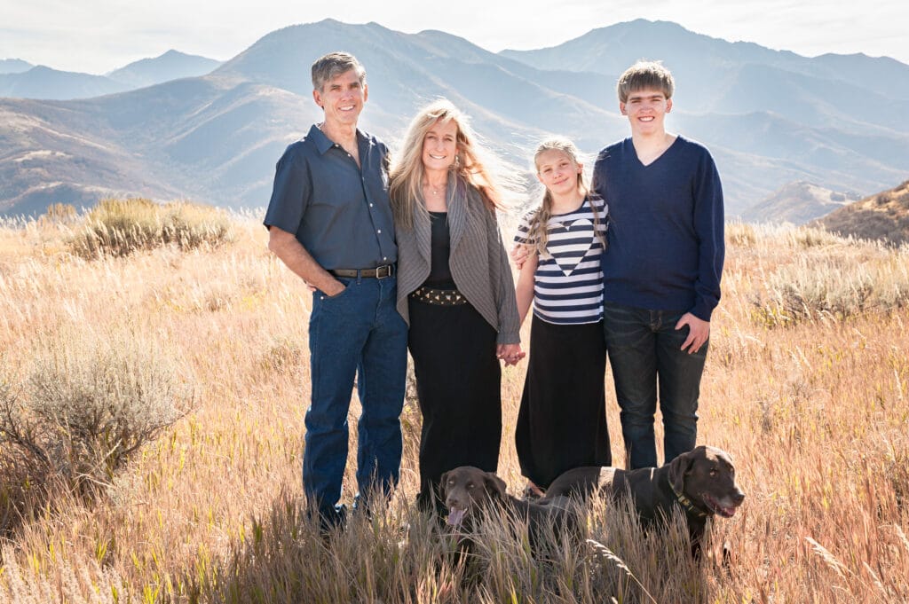 A man, woman, son, daughter, and two dogs pose in front of hazy mountains for their outdoor family portraits.