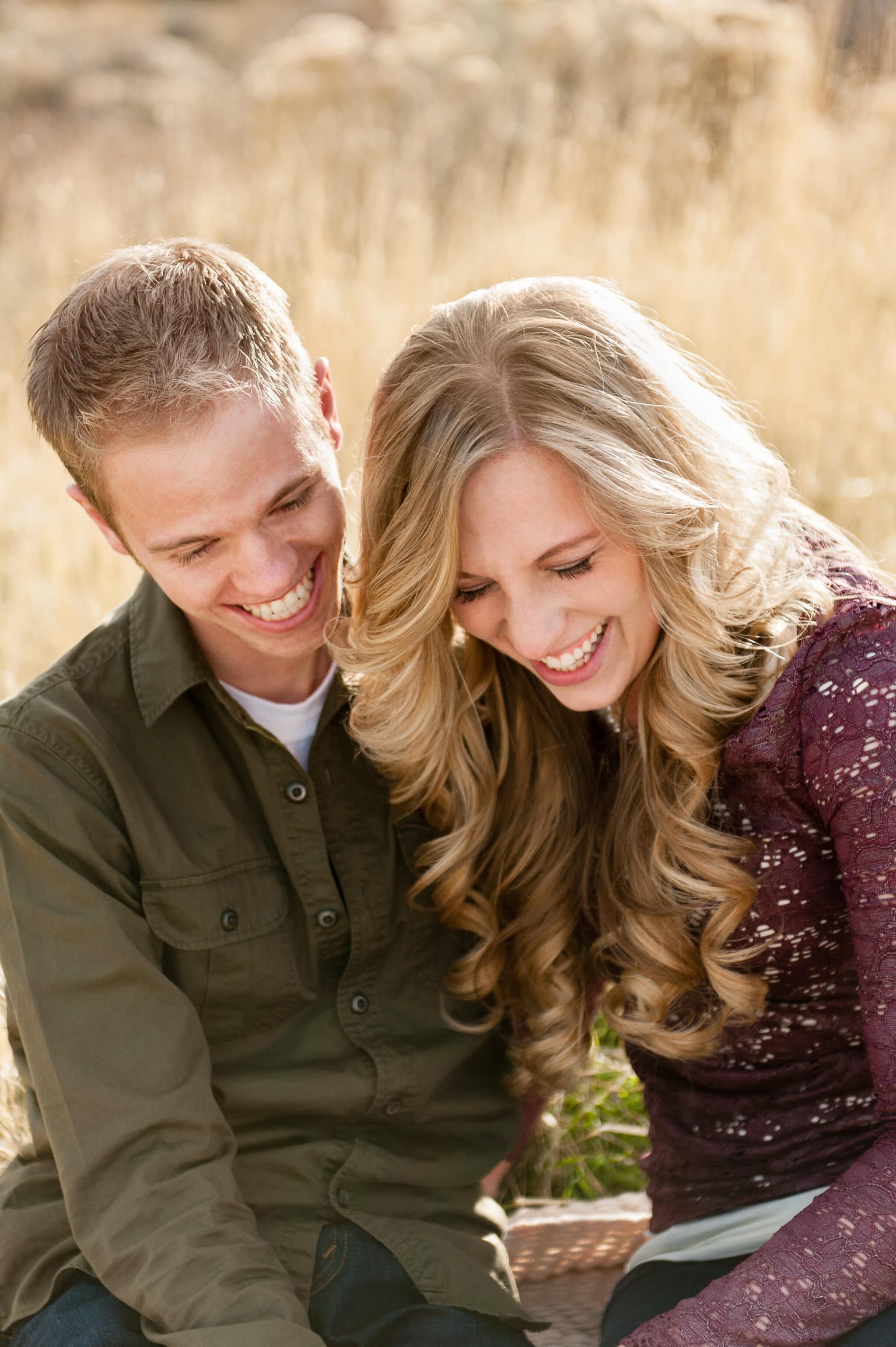 A man looks on as his girlfriend laughs during their engagement photo session.