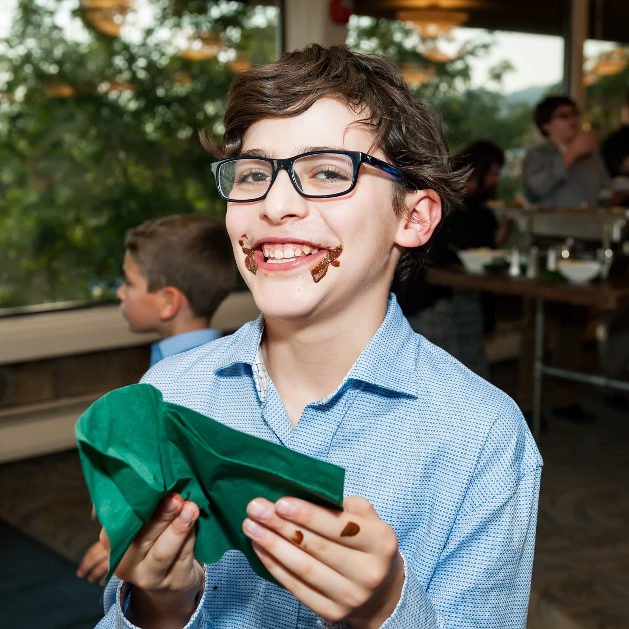 A young man uses a napkin to remove chocolate from his mouth after tasting decadent desserts.