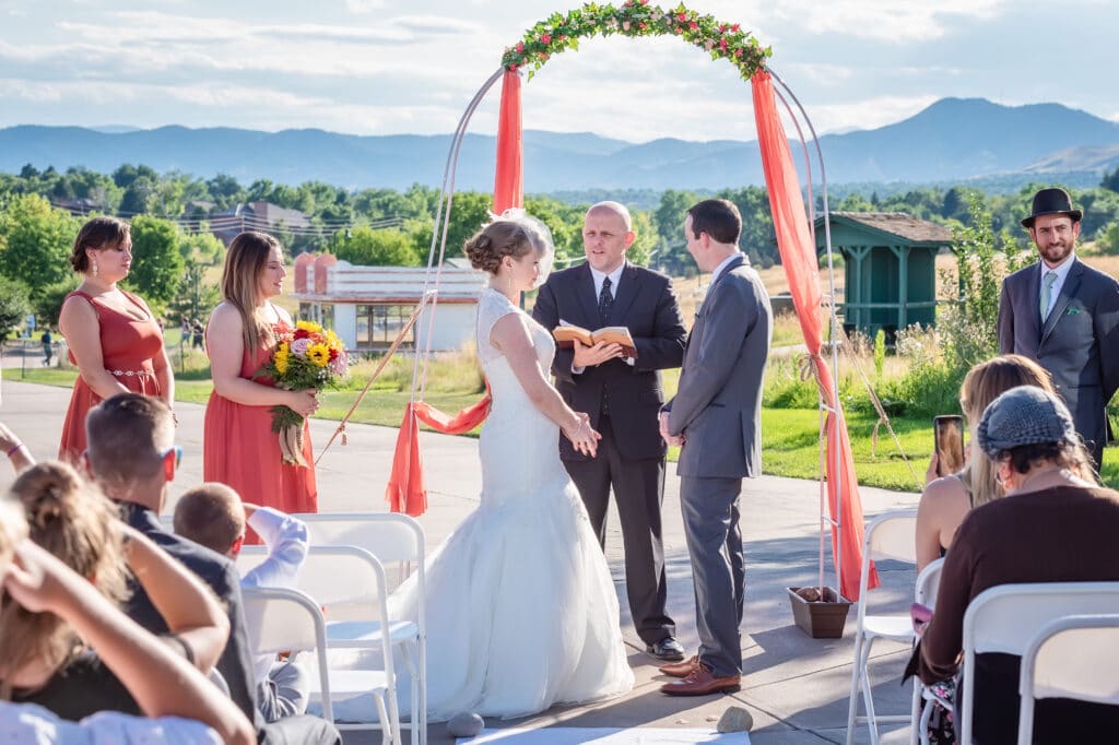 A bride and groom under a colorful peach wedding arch at the historic Lakewood Heritage Center.