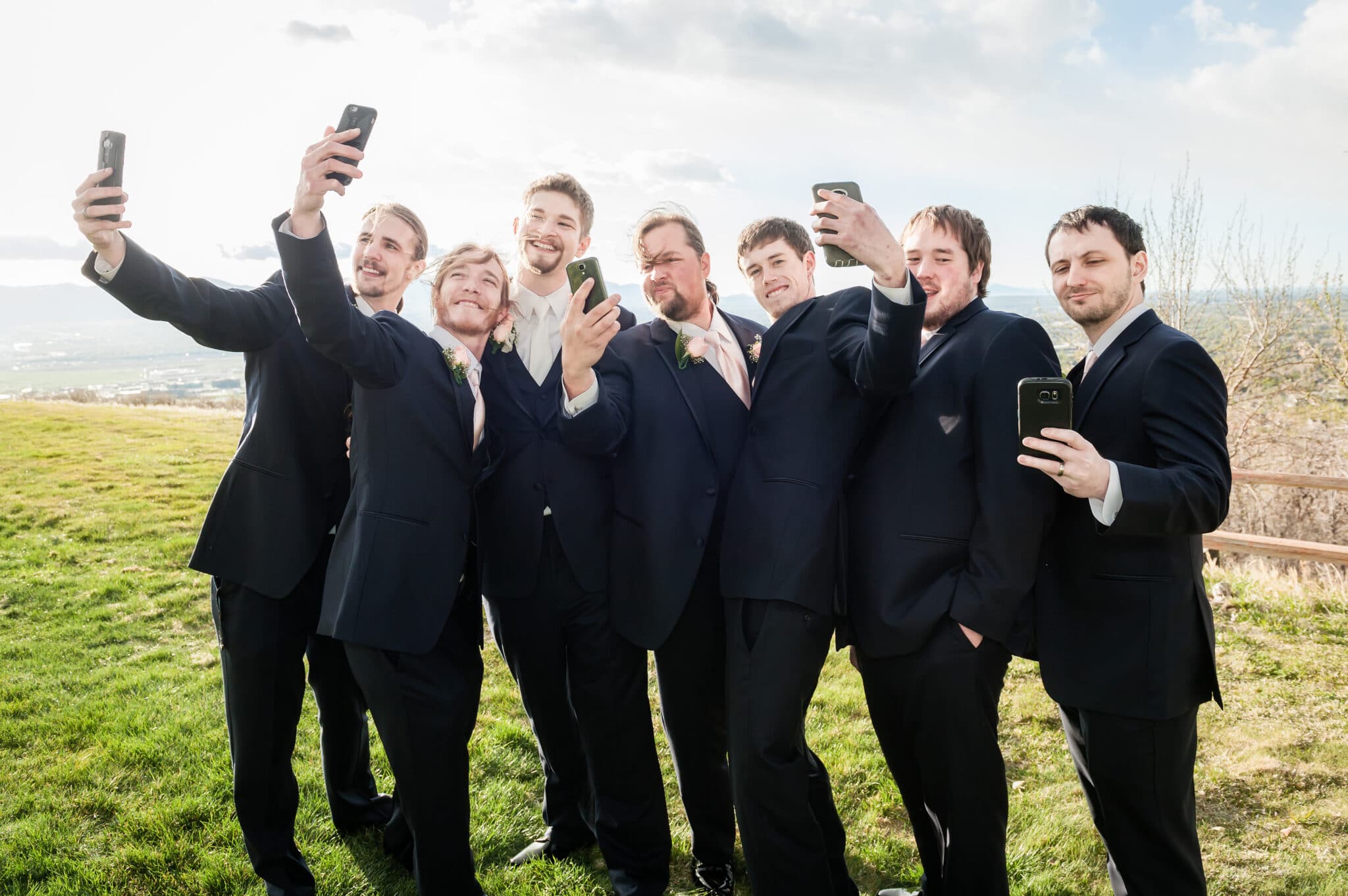 Groomsmen take selfies of themselves during an outdoor wedding at a public golf course.