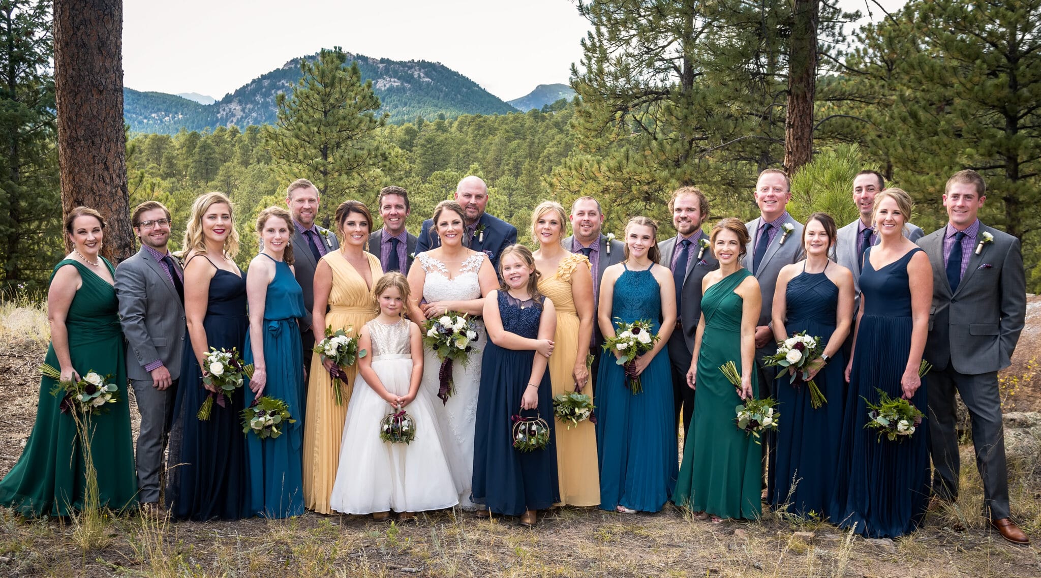Nineteen member wedding party in complementary jewel tones that include burgundy, gold, emerald green, inky blue, and navy.